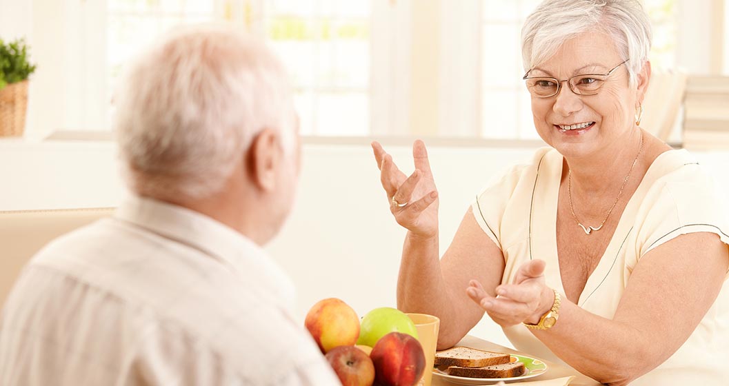 An older woman chats to an older man while sitting at a table