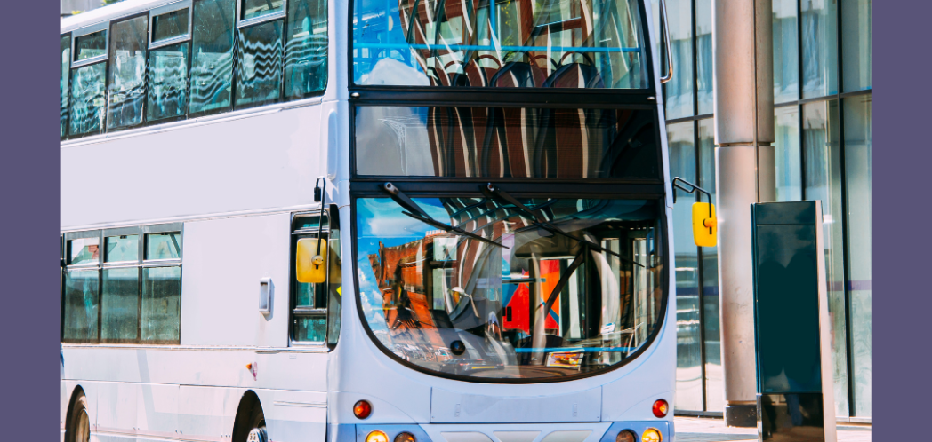 Double decker bus driving along road with glass fronted office building in background