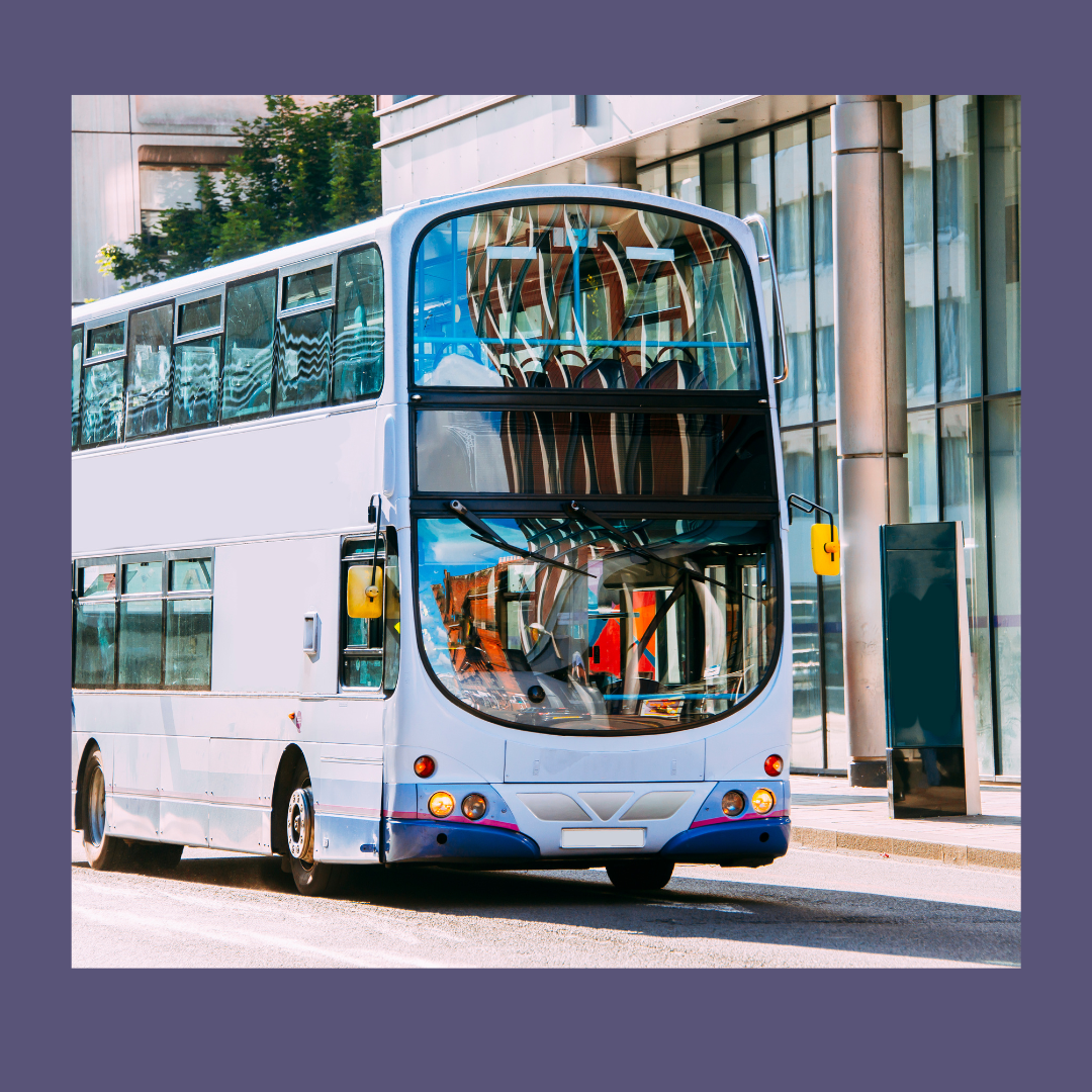 Double decker bus driving along road with glass fronted office building in background