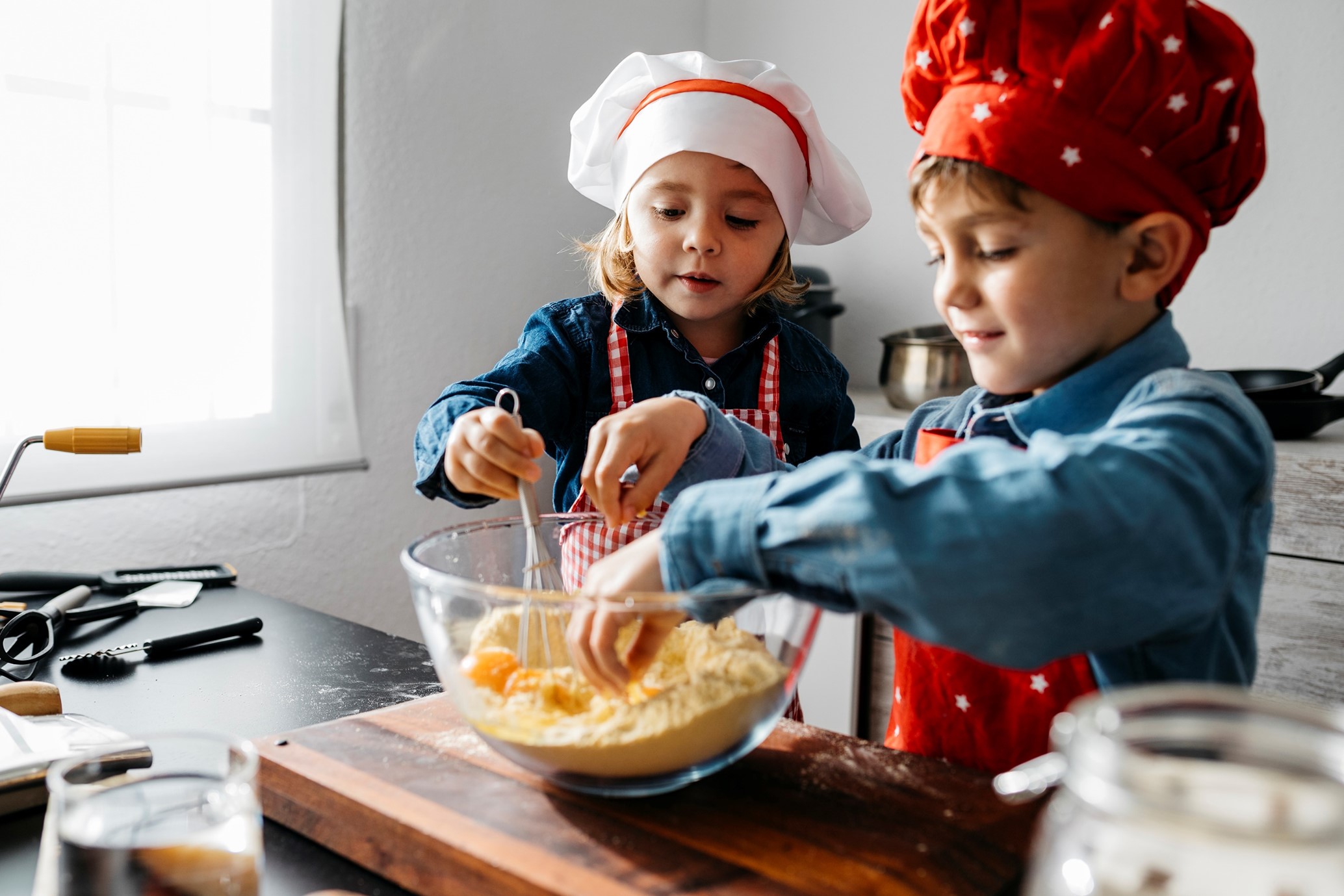 a boy and a girl wearing their chef hats with hands in a mixing bowl