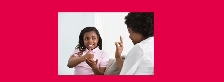 A young black girl smiles and uses sign language with her mother